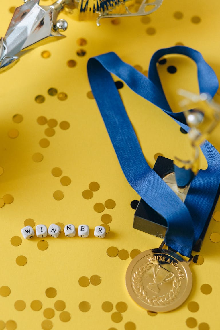 Gold medal and winner's trophy on a vibrant yellow confetti background, symbolizing success and victory.